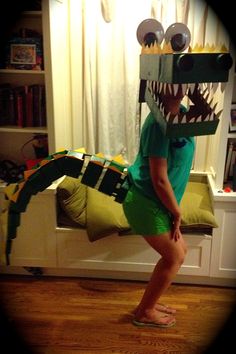 a young boy wearing a paper mask and green shorts standing in front of a bed