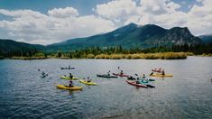 a group of people riding kayaks on top of a lake next to tall mountains