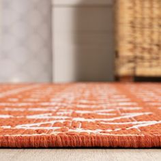 an orange and white rug on the floor in front of a wicker basket,