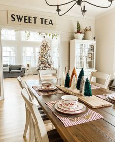 a dining room table set for christmas with plates and place settings on the wooden table