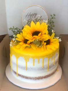 a yellow and white cake with sunflowers in the middle on a cardboard box