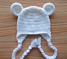 a white crocheted hat with ears on top of a wooden table next to a pair of scissors