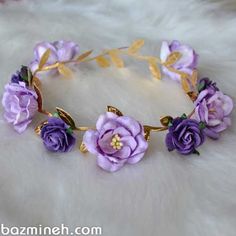 a purple flower crown with gold leaves and flowers on the headband is laying on a white fur surface