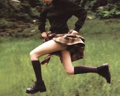 a woman is running in the grass with her skirt pulled back and boots on,