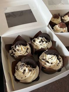 four cupcakes with white frosting and oreo cookies in a cardboard box