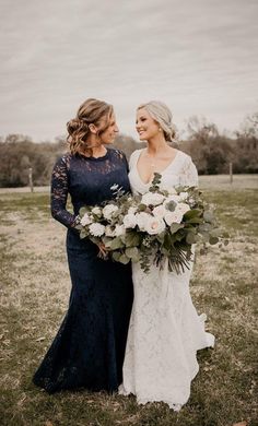 two women standing next to each other in a field with flowers on their wedding day