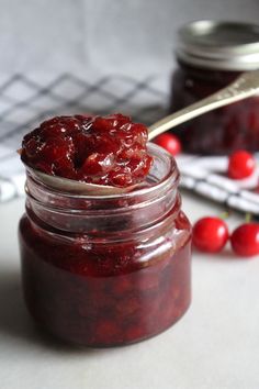 a jar filled with cranberry sauce sitting on top of a table next to some cherries