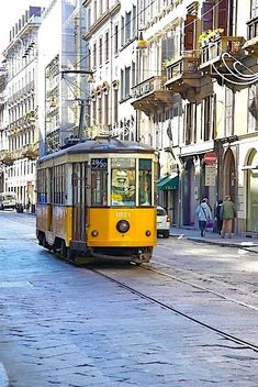 a yellow trolley car traveling down a street next to tall buildings