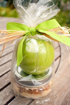 an apple is wrapped in plastic and sitting on a wooden table with a green bow