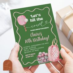 a person holding up a green birthday card with pink decorations on it and presents in the background