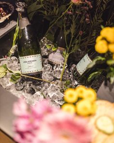 two bottles of wine sitting on top of an ice covered table with flowers in the background