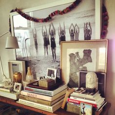 a table topped with books and pictures next to a wall mounted art piece on top of a wooden shelf