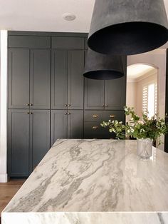 a large kitchen with marble counter tops and black cabinetry, along with hanging lights