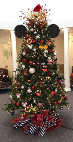 a decorated christmas tree with mickey mouse ears on top and red bows around the base