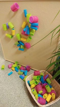 a basket filled with lots of different colored plastic toys next to a plant on the floor