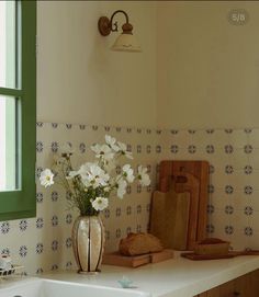 a white sink sitting under a window next to a wooden cutting board with flowers in it