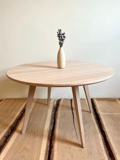 a wooden table with a white vase on top and some small flowers in the middle