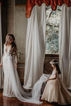 two brides standing in front of a window with white curtains and sheer drapes