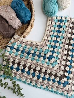 a crocheted blanket next to two balls of yarn and a basket with green leaves