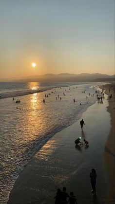 many people are on the beach as the sun is setting in the sky over the water