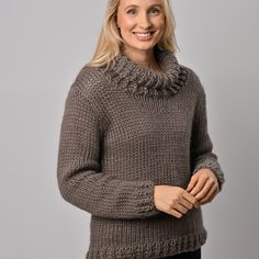 a woman wearing a brown sweater and black pants smiles at the camera while standing in front of a gray background