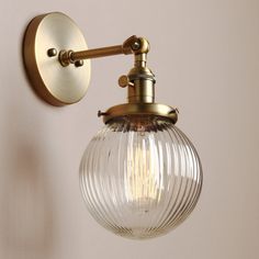 a wall light with a glass globe shade on it's arm and an antique brass finish