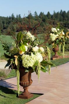 there are three vases with flowers in them on the grass near a path that leads to a golf course