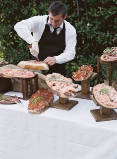 a man in an apron preparing pizzas on wooden trays at a buffet table