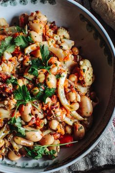 a white bowl filled with pasta and vegetables on top of a table next to bread