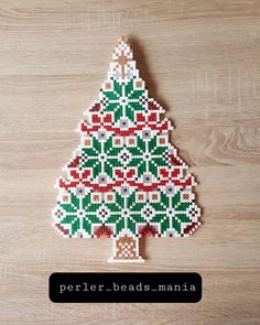 a cross stitch christmas tree ornament on a wooden surface with the words perler beads mania written below it