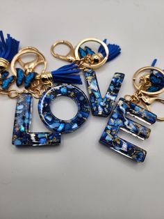 the word love spelled with blue beads and tassels on a white surface, surrounded by gold - plated key chains