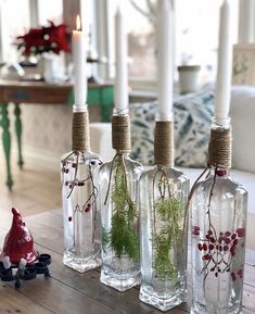 three glass bottles with plants in them sitting on a table next to two white candles