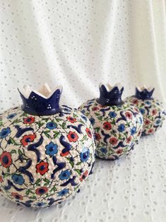 three decorative vases with blue and red flowers on them sitting on a white tablecloth