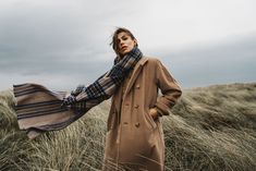 a woman standing in tall grass wearing a coat and scarf