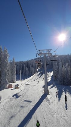 two people skiing down a snow covered slope under a ski lift with trees in the background