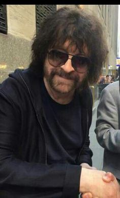 a man with long hair and sunglasses sitting on a bench in front of a building