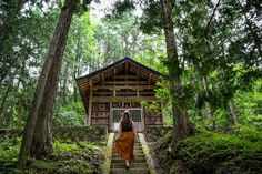 a woman in an orange dress walking up stairs to a small wooden structure surrounded by trees