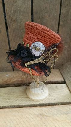 an orange and black hat with some scissors on it's head sitting on a stand