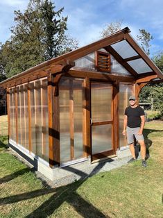 a man standing in front of a small wooden structure with glass doors on the side