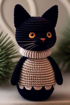 a crocheted black cat sitting on top of a table next to a pine tree