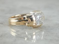 a gold ring with a princess cut diamond set in the center on a marble surface