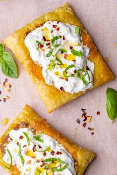 two pieces of pizza with cream cheese and green leaves on top, sitting on a piece of parchment paper