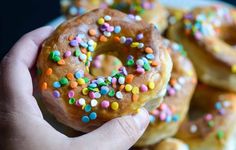 a hand holding a donut with sprinkles on it