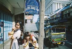 two young women standing next to a bus stop on the side of a city street