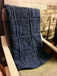 a blue crocheted blanket sitting on top of a chair next to a wooden wall