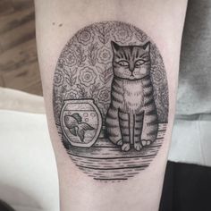 a black and white cat sitting next to a fish bowl on the arm with goldfish in it