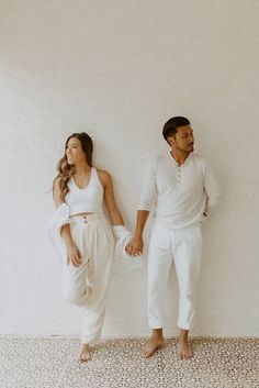 a man and woman standing next to each other in white outfits, holding hands with one another