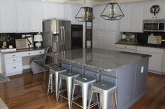 a large kitchen with an island and stools in the center, surrounded by white cabinets