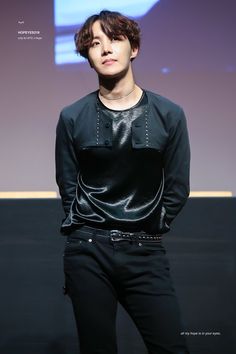 a young man standing in front of a screen wearing black pants and a black shirt