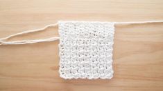 a white crochet square is tied up on a wooden surface with yarn around it